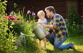 Middle age man and his little son watering flowers in the garden at summer sunny day Middle age man and his little son watering flowers in the garden at summer sunny day